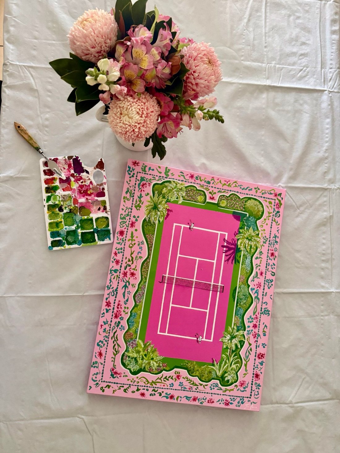 The Tennis Court painting laid flat beside a paint palette and pink flowers